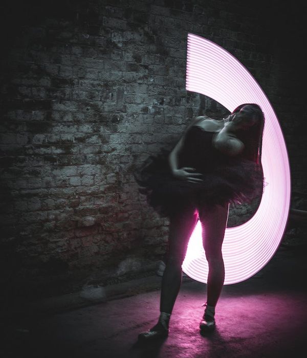 Woman in a graceful yoga pose against a dark background with pink light accents.